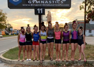 Smiling young girl gymnasts outside in front of Synergy Gymnastics sign